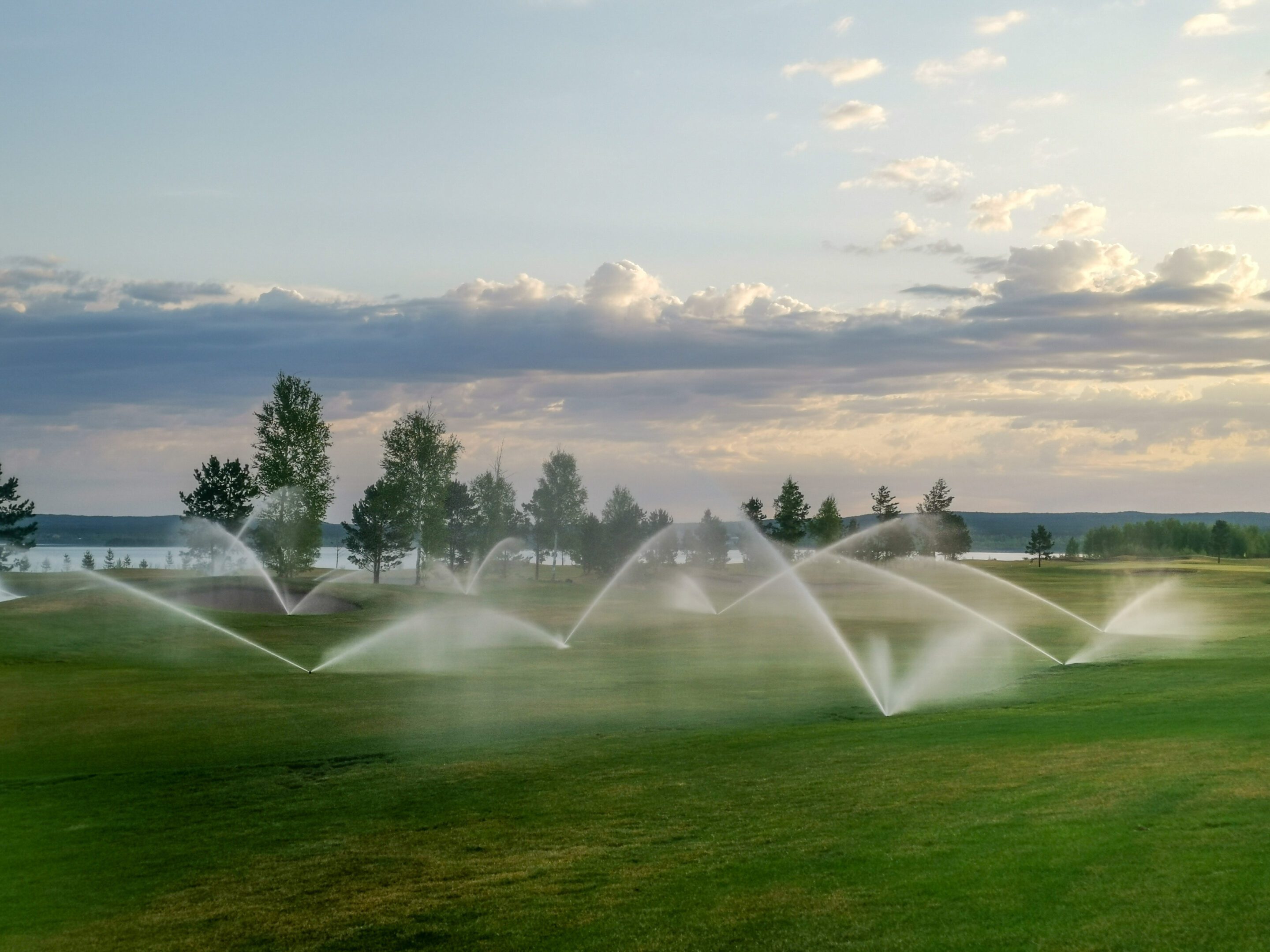 Sprinklers watering a lush green field under a cloudy sky.